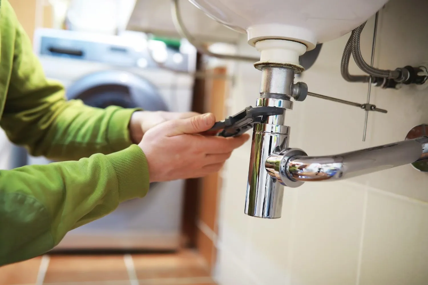 Hands tightening a sink drain pipe with a wrench